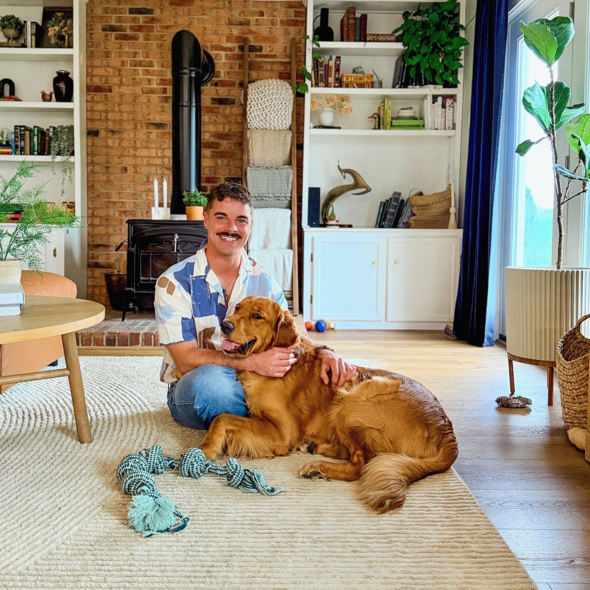 Matt sitting with a dog in a sunlit living room.